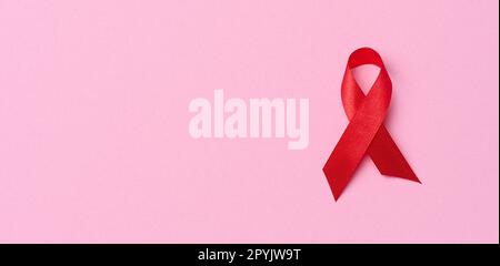 A silk red ribbon in the form of a bow on a pink background, a symbol of the fight against AIDS and a sign of solidarity and support Stock Photo