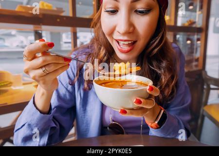 Happy girl eating spicy thai soup Tom Yam in authentic restaurant Stock Photo