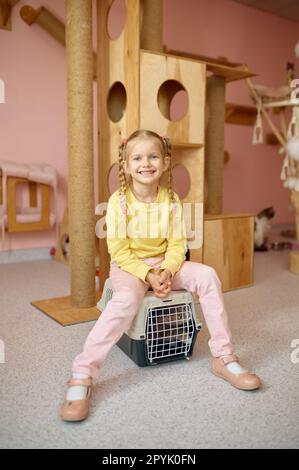 Portrait of cheerful girl sitting on cage with cat over animal shelter Stock Photo