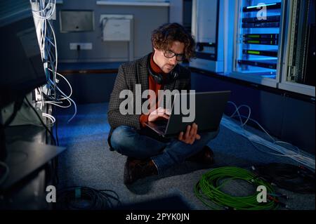 A system administrator working in server room using laptop Stock Photo