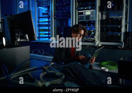 Male system administrator working in server room using laptop Stock Photo