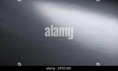 Long flare of light on shiny gray paper. A light spot on a monochrome surface that reflects light. Abstract monochrome background. Strip from top left to right down Stock Photo