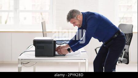 Irritated Businessman Looking At Paper Stuck In Printer Stock Photo