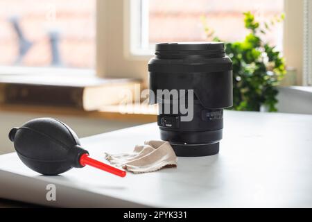 Lens on desk with cleaning tools for DSLR and Mirrorless cameras. Cleaning kit for cmos surface. Air blower, swab, isopropyl alcohol dropper and microfyber cloths. Lens and camera cleaning solution for professionals. Stock Photo