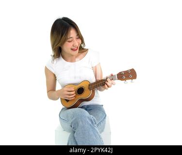Young asian woman in white t-shirt and jean playing an Ukulele guitar. Portrait on white background with studio light. Stock Photo
