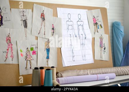 Pattern for cloth are pasted on the board in the sewing room. Rolls of cloth and multi-colored threads are on the table. Fashion designer room. Stock Photo