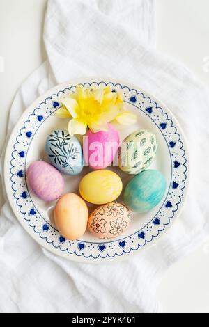 Easter eggs are painted in different colors and patterns on the plate. Top view, Easter celebration concept. Stock Photo