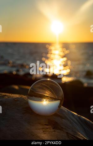 Ball made of glass lies on a stone in which the beach and the sea are ...