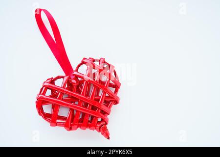 Red braided heart with a silk ribbon on a white background. Valentine's Day. copyspace. A nice souvenir - a pendant at an angle. Stock Photo