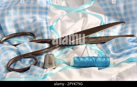 Spool of Blue Thread, Thimble and Needle on Blue and White Fabric Stock Photo