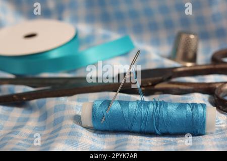 Spool of Blue Thread, Thimble and Needle on Blue and White Fabric Stock Photo