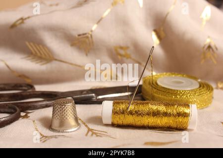 Spool of Gold Thread and Scissors With Thimble on Metallic Fabric Stock Photo