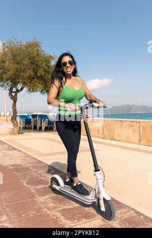 Woman riding electric scooter, happy and summer ride at tropical island beach resort for vacation. City, street and eco friendly transport, fun on escooter on holiday in mallorca,balearic island Stock Photo