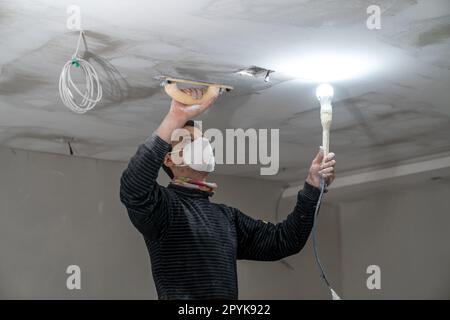 sanding a plasterboard ceiling in a new building with a trowel Stock Photo