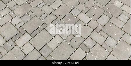 Cobbled street of the old city, lined with square and rectangular stone tiles in a chaotic manner. Soft gray color. The texture of the stone. Geometric pattern. Stock Photo