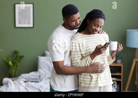 Happy lovely couple reading message on smartphone and drinking coffee while they spending time at home Stock Photo