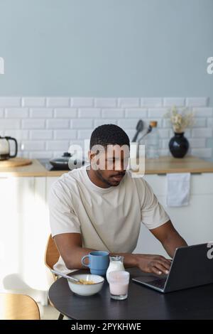 African American man working on laptop during breakfast while sitting at table in the kitchen Stock Photo