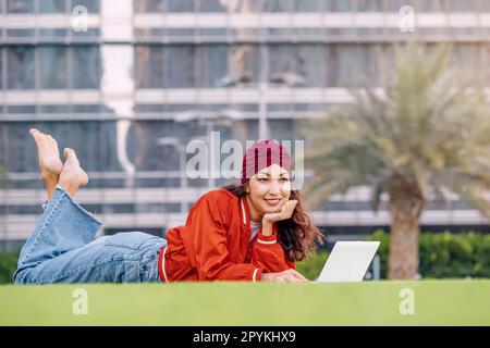 In a peaceful park setting, a studious young woman works on her laptop, surrounded by nature's beauty and inspiration. Stock Photo