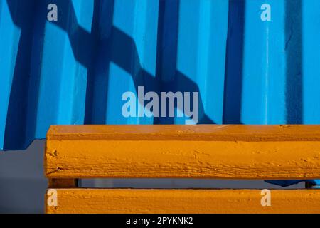 Bright blue corrugated roofing panel with bright orange pained timber in front with diagonal show over the blue Stock Photo