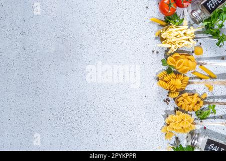 Various dried  spaghetti, noodles, pasta  set in spoons on white table background. Different shapes types raw italian pasta with herbs, olive oil, tom Stock Photo