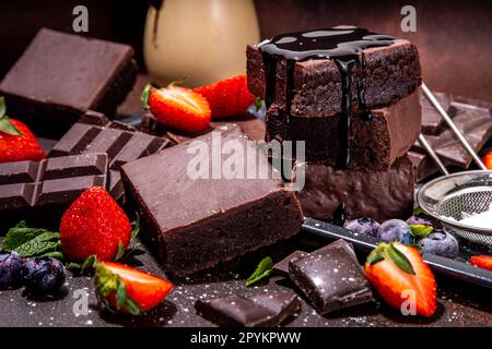 Dark chocolate brownies with berries. Stack of homemade brownie cake cookies with chocolate sauce drizzled on it and fresh strawberry, blueberry, on d Stock Photo