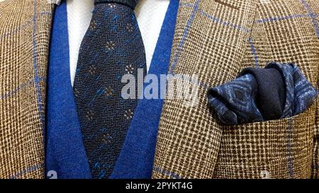 Elegant men's outfit, showcasing a brown checkered suit, a dark blue tie with floral pattern and a matching pocket square, accompanied by a blue sweat Stock Photo