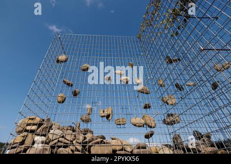 Wire Gabion Rock Fence. Stone wall texture, rocks behind metal grid fence background and beautiful blue sky. Stock Photo
