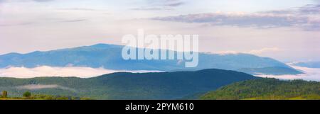 colorful foggy sunrise in mountainous rural area. panorama with forested hills covered in morning mist. dramatic clouds above the distant ridge. trave Stock Photo