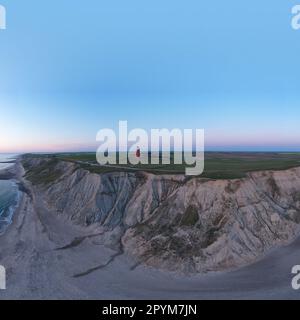 Panoramic aerial shot of a red lighthouse on a seaside cliff during sunset. Angled view taken with a drone of a navigation lighthouse on top of a clif Stock Photo