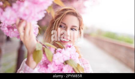 Beautiful 30s caucasian woman holding cherry blossom at springtime, outdoors Stock Photo