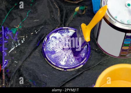 a large can of paint,  on a black canvas,  a yellow brush next to the jar,  the bristles are blue from the blue paint, the brush handle is on the jar. Stock Photo