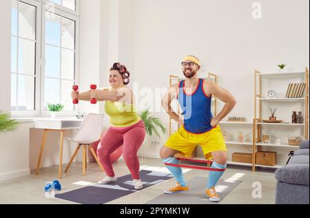 Overweight fat woman with funny bearded man in bright sportswear doing exercises at home together. Stock Photo
