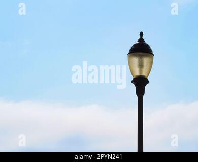 Old-fashioned lamp post street light in daytime against light blue sky with clouds, copy space. Stock Photo