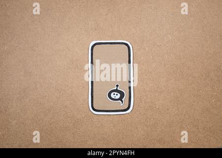Mobile phone made our of paper with bot in the speech bubble on the display, concept of chatting with bot. Asking question to AI. Cardboard smartphone Stock Photo