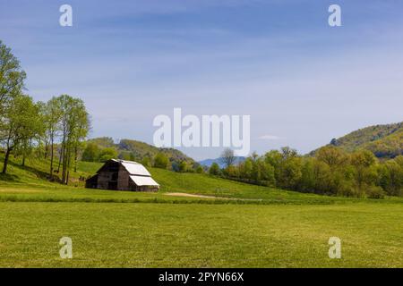 Springtime agriculture landscape with trees, hills and a barn under semi cloutdy skies. Stock Photo
