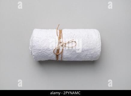Rolled white towel tied with a rope on gray paper background. Stock Photo
