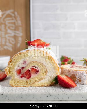 Summer Strawberry dessert with fresh baked swiss roll filled with whipped cream and marinated strawberries. Served on white kitchen table background Stock Photo