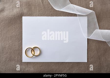 Wedding announcement background with gold rings in paper cutout on brown cloth and detail of white ribbon. Top view. Stock Photo