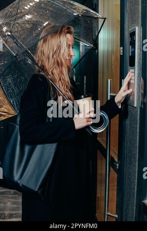 Woman dialing a number on the on video intercom at entrance of apartment building in the night Stock Photo