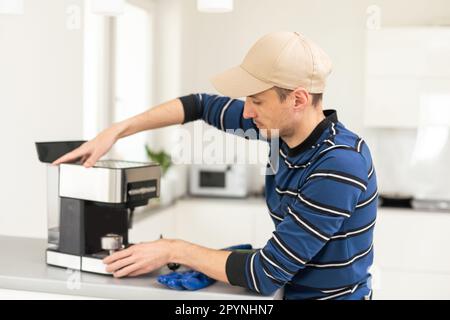 Professional young repairman repairs a coffee maker. Handsome worker in uniform repairing coffee machine in a workshop. Stock Photo