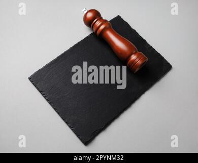 Pepper mill and black stone slate plate on gray paper background. Stock Photo