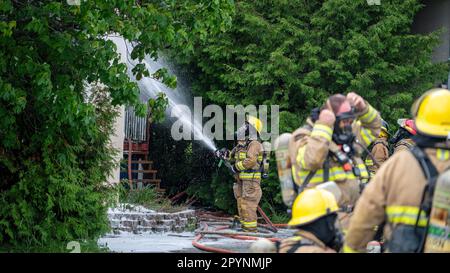 Firefighter fighting a house fire with a group of firefighters preparing to fight Stock Photo