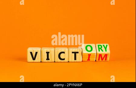 From victim to victory symbol. Businessman turns wooden cubes and changes concept words Victim to Victory. Beautiful orange background. Business suppo Stock Photo