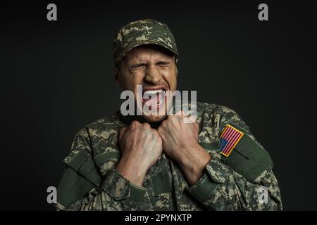 stressed soldier in uniform with USA flag screaming while suffering from panic attacks isolated on black,stock image Stock Photo