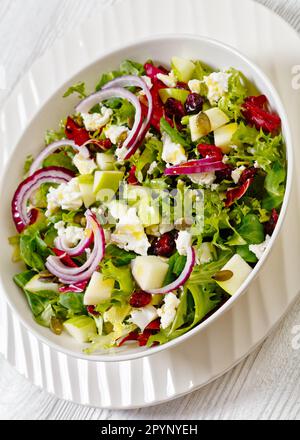 close-up of Green Salad with Apples, Goat Cheese, Cranberries, Red Onion and Pepitas in white bowl Stock Photo