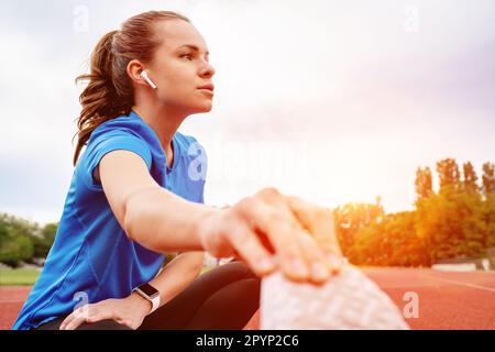 Athlete woman with wireless earphones doing stretching exercise after running workout. Stock Photo