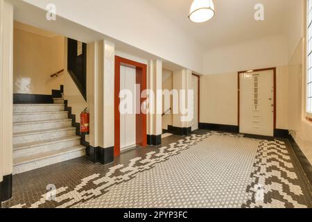 an empty room with tiled floor and red door in the middle, white walls on both sides, and black trim around the doors Stock Photo