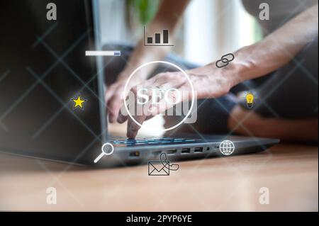 Virtual interface with a glowing SEO  sign with female hands working on laptop computer in background. Conceptual image of search engine optimization Stock Photo
