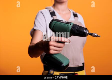 Construction worker holding cordless drilling gun over background, advertising electric power drill nail gun used in building and refusrbishment project. Screwing gun and renovating tools. Close up. Stock Photo