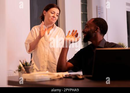 Colleagues giving high five, celebrating success, coworkers teamwork, man and woman working on laptop in office at night. Two employees checking company report together in coworking space Stock Photo
